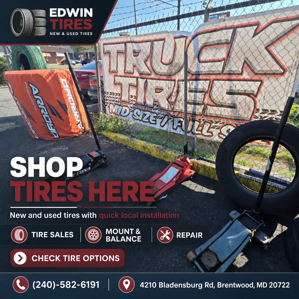 Edwin Tires outdoor display with tire jacks, spare tires, and a 'Truck Tires' banner behind a chain-link fence.